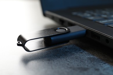 Photo of USB flash drive connected to laptop on dark grey table, closeup