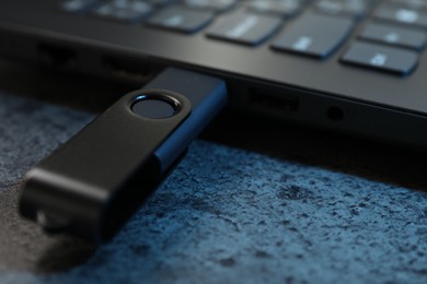 Photo of USB flash drive connected to laptop on dark grey table, closeup