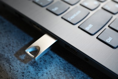 Photo of USB flash drive connected to laptop on dark grey table, closeup