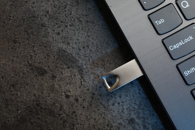 Photo of USB flash drive connected to laptop on dark grey table, top view. Space for text