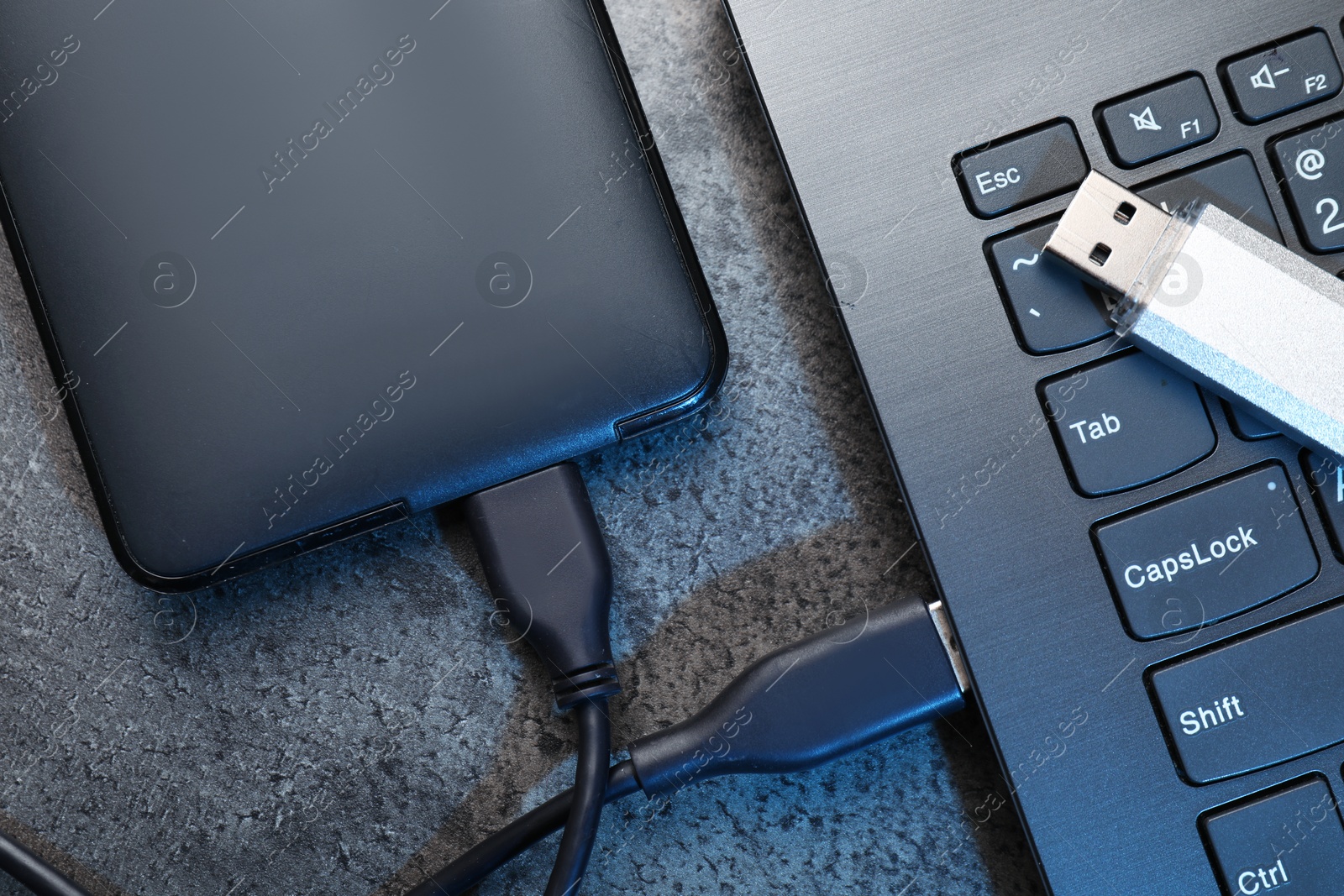 USB flash drive, hard disk drive with cable and laptop on dark grey table, flat lay Photo of USB flash drive, hard disk drive with cable and laptop on dark grey table, flat lay