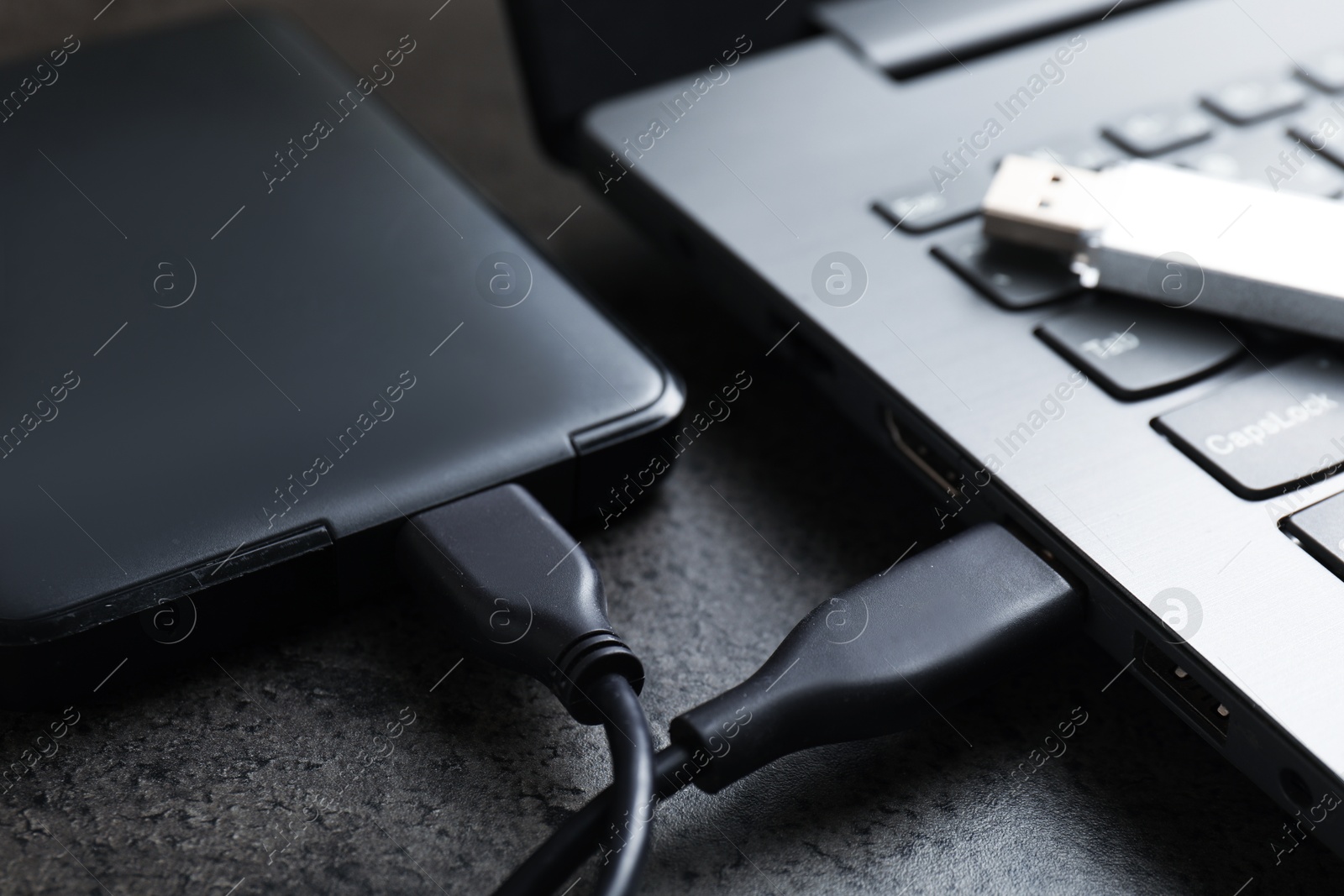 USB flash drive, hard disk drive with cable and laptop on dark grey table, closeup Photo of USB flash drive, hard disk drive with cable and laptop on dark grey table, closeup