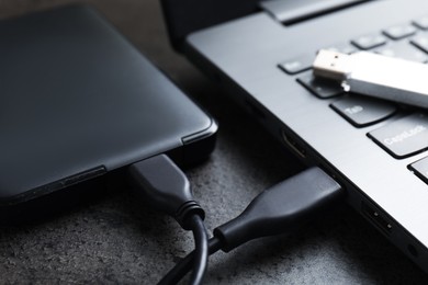 Photo of USB flash drive, hard disk drive with cable and laptop on dark grey table, closeup