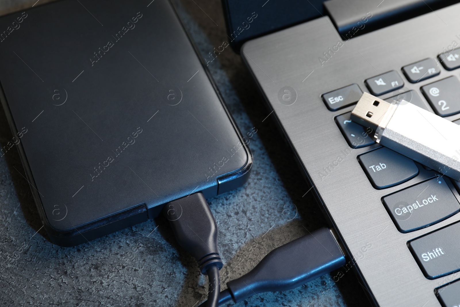 USB flash drive, hard disk drive with cable and laptop on dark grey table, closeup Photo of USB flash drive, hard disk drive with cable and laptop on dark grey table, closeup