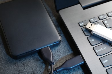 Photo of USB flash drive, hard disk drive with cable and laptop on dark grey table, closeup