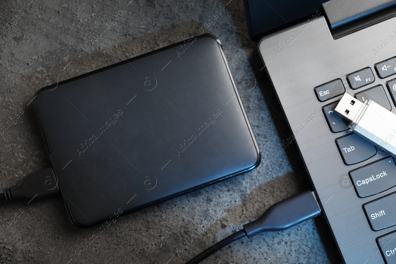 USB flash drive, hard disk drive with cable and laptop on dark grey table, flat lay Photo of USB flash drive, hard disk drive with cable and laptop on dark grey table, flat lay