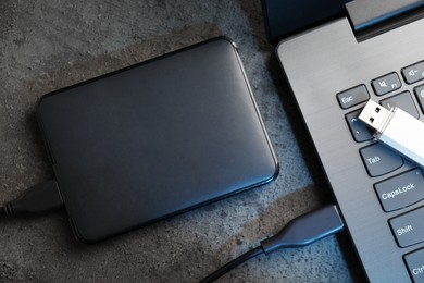 Photo of USB flash drive, hard disk drive with cable and laptop on dark grey table, flat lay