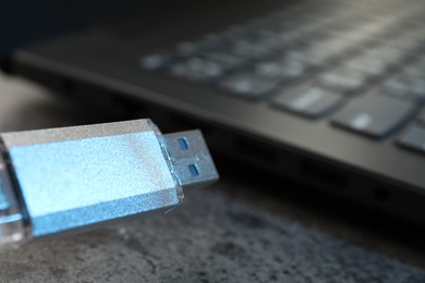 Photo of USB flash drive and laptop on dark grey table, closeup
