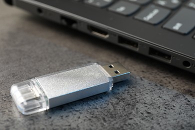 Photo of USB flash drive and laptop on dark grey table, closeup