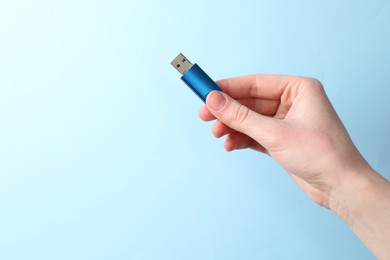 Photo of Woman holding USB flash drive on light blue background, closeup. Space for text