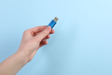 Photo of Woman holding USB flash drive on light blue background, closeup. Space for text