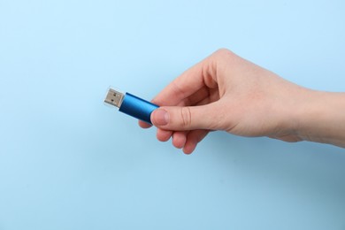 Photo of Woman holding USB flash drive on light blue background, closeup