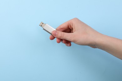 Photo of Woman holding USB flash drive on light blue background, closeup. Space for text