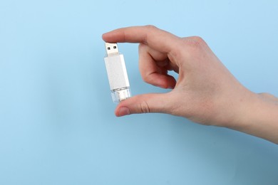 Photo of Woman holding USB flash drive on light blue background, closeup. Space for text