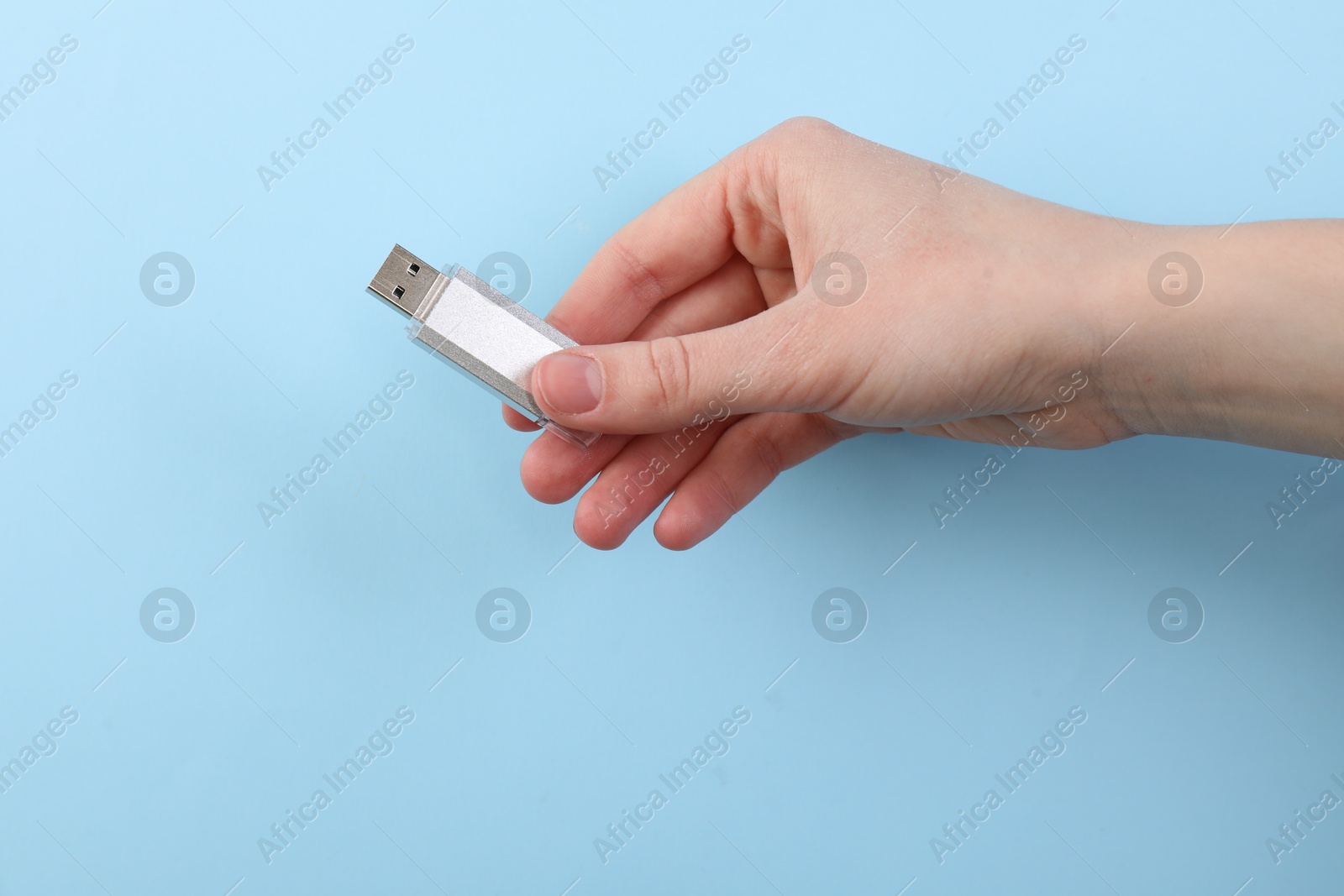 Woman holding USB flash drive on light blue background, closeup Photo of Woman holding USB flash drive on light blue background, closeup