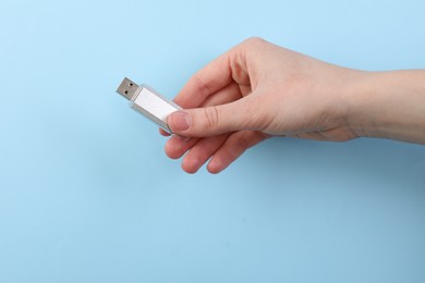 Photo of Woman holding USB flash drive on light blue background, closeup