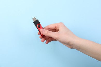 Photo of Woman holding USB flash drive on light blue background, closeup