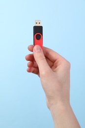 Photo of Woman holding USB flash drive on light blue background, closeup