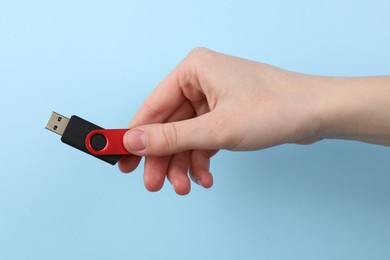 Photo of Woman holding USB flash drive on light blue background, closeup