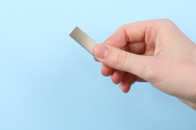 Photo of Woman holding USB flash drive on light blue background, closeup. Space for text