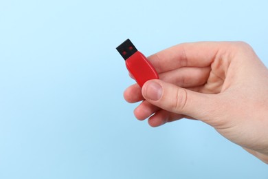 Photo of Woman holding USB flash drive on light blue background, closeup. Space for text