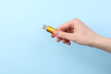 Photo of Woman holding USB flash drive on light blue background, closeup. Space for text