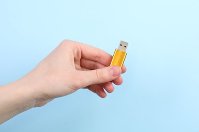Photo of Woman holding USB flash drive on light blue background, closeup. Space for text