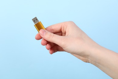 Photo of Woman holding USB flash drive on light blue background, closeup