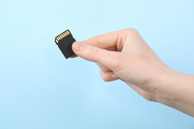 Photo of Woman holding SD memory card on light blue background, closeup