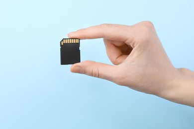 Photo of Woman holding SD memory card on light blue background, closeup