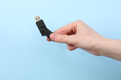 Photo of Woman holding USB flash drive on light blue background, closeup