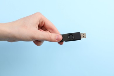 Photo of Woman holding USB flash drive on light blue background, closeup