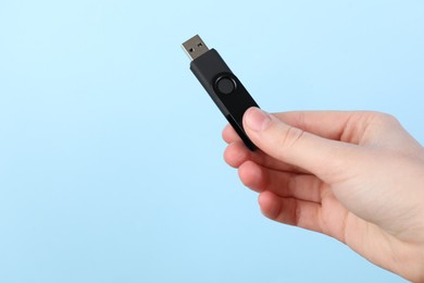Photo of Woman holding USB flash drive on light blue background, closeup. Space for text