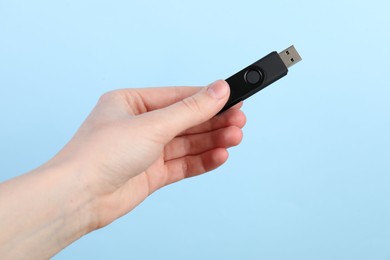 Photo of Woman holding USB flash drive on light blue background, closeup