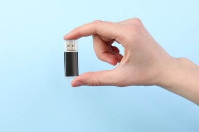 Photo of Woman holding USB flash drive on light blue background, closeup
