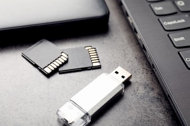 Photo of SD memory cards, USB flash drive, hard disk drive and laptop on dark grey table, closeup