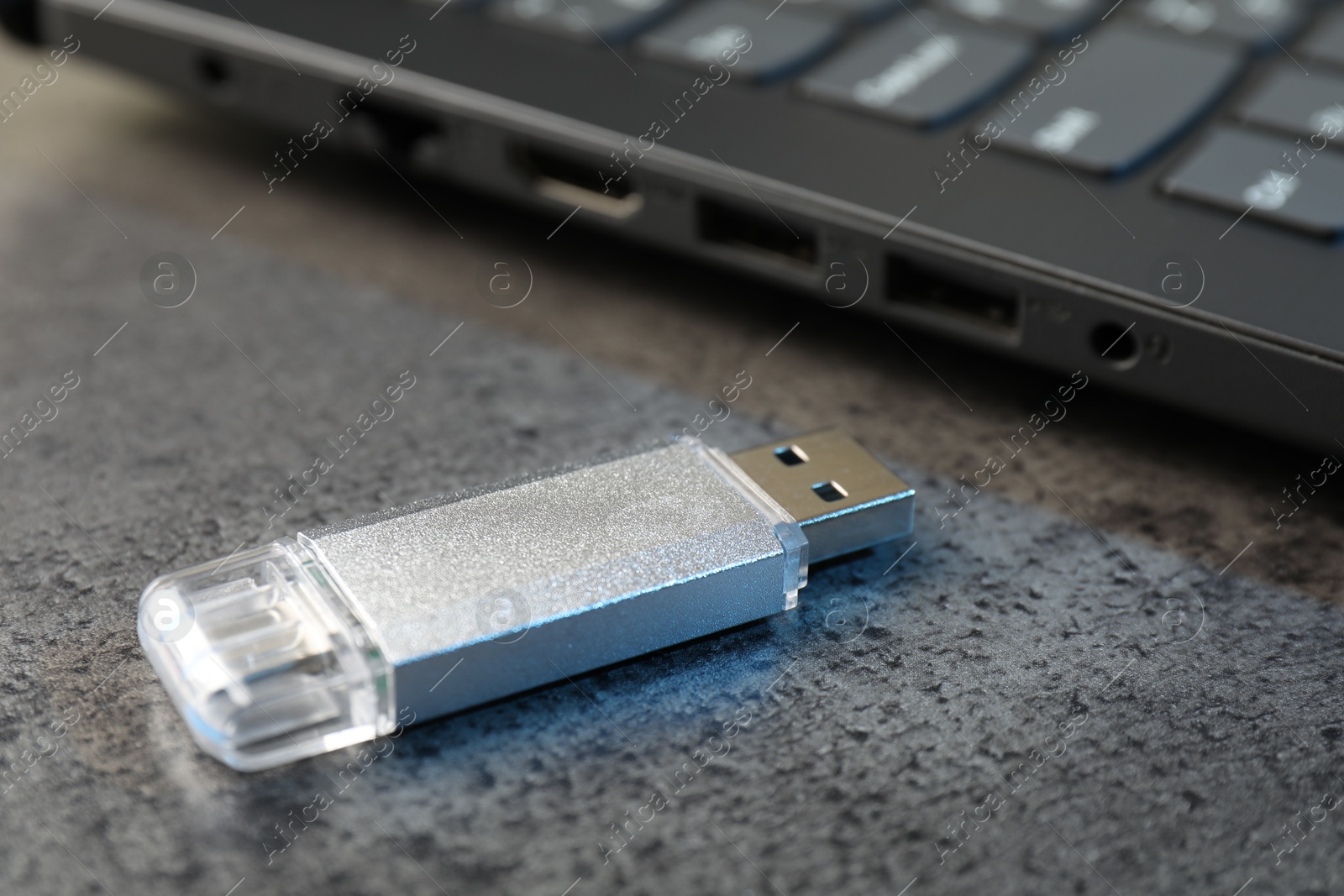 USB flash drive and laptop on dark grey table, closeup Photo of USB flash drive and laptop on dark grey table, closeup