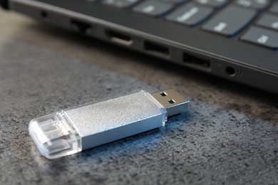 Photo of USB flash drive and laptop on dark grey table, closeup