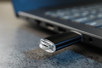 Photo of USB flash drive connected to laptop on dark grey table, closeup