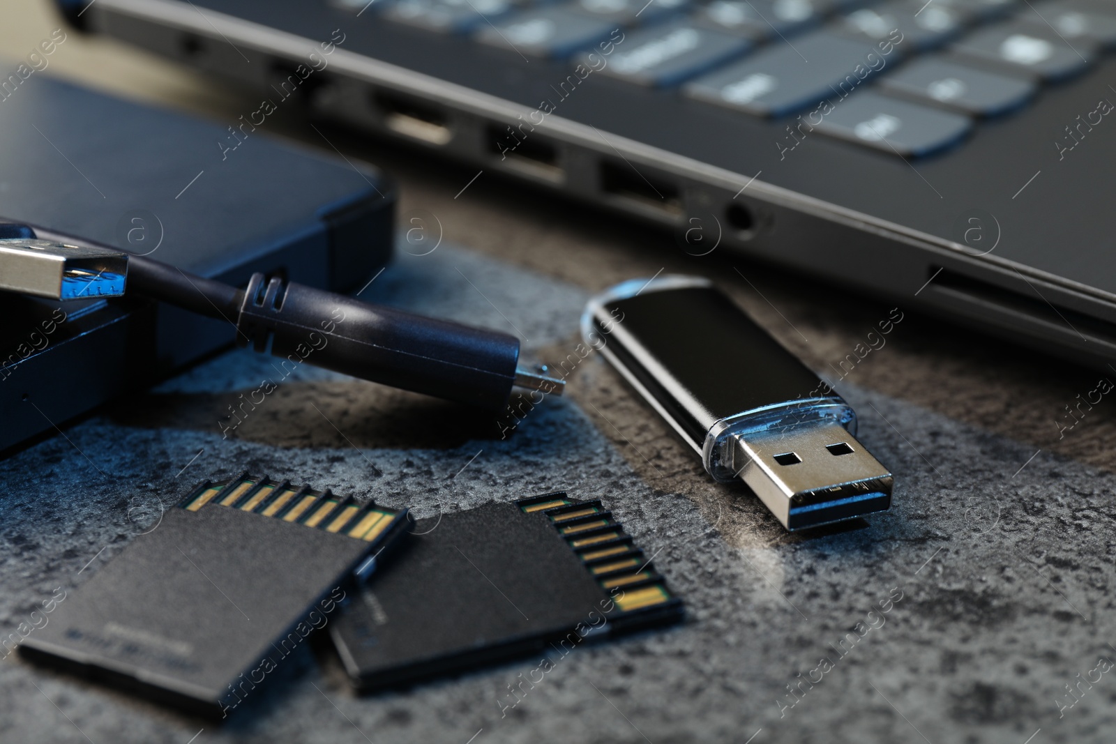 SD memory cards, USB flash drive, hard disk drive with cable and laptop on dark grey table, closeup Photo of SD memory cards, USB flash drive, hard disk drive with cable and laptop on dark grey table, closeup