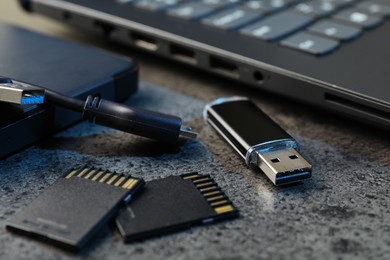 Photo of SD memory cards, USB flash drive, hard disk drive with cable and laptop on dark grey table, closeup