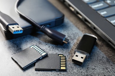 Photo of SD memory cards, USB flash drive, hard disk drive with cable and laptop on dark grey table, closeup