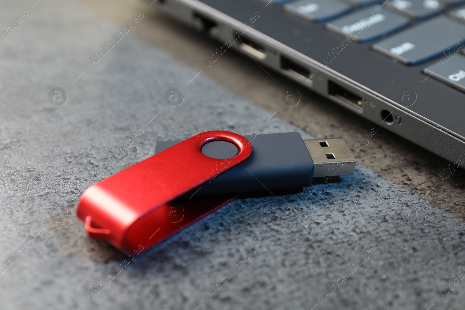 USB flash drive and laptop on dark grey table, closeup Photo of USB flash drive and laptop on dark grey table, closeup