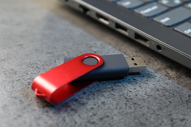 Photo of USB flash drive and laptop on dark grey table, closeup