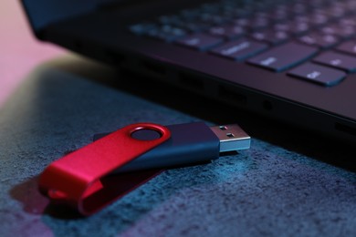 Photo of USB flash drive and laptop on dark grey table, closeup