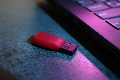 Photo of USB flash drive and laptop on dark grey table, closeup