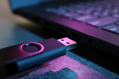 Photo of USB flash drive and laptop on dark grey table, closeup