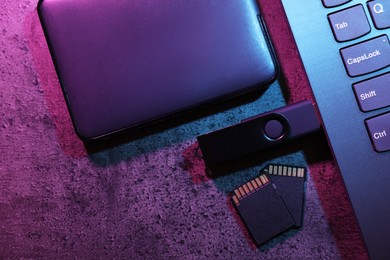 Photo of SD memory cards, USB flash drive, hard disk drive and laptop on dark grey table, flat lay