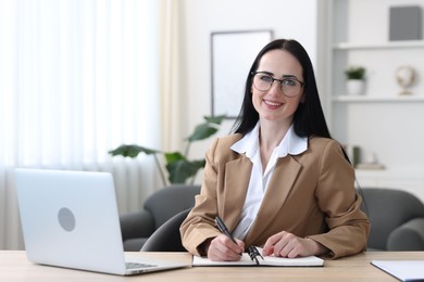 Photo of Professional psychologist taking notes while working with laptop at table in office