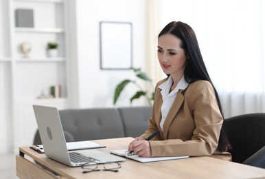 Photo of Professional psychologist taking notes while working with laptop at table in office